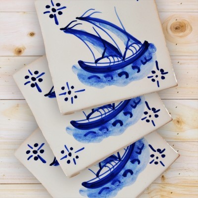 Três azulejos de cerâmica com desenho de barco azul e padrão tradicional nos cantos