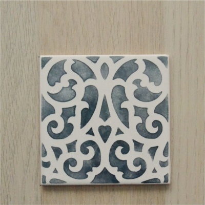 Azulejo quadrado branco com padrão ornamental cinza escuro sobre madeira clara