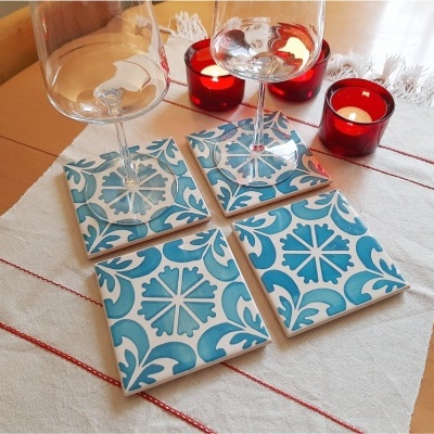 Quatro bases de copos em cerâmica azul e branca com padrão tradicional, copos de vidro e velas vermelhas sobre mesa de madeira