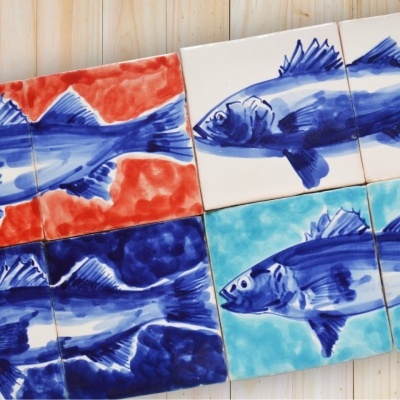 Azulejos cerâmicos com peixes azuis em fundos coloridos sobre madeira clara