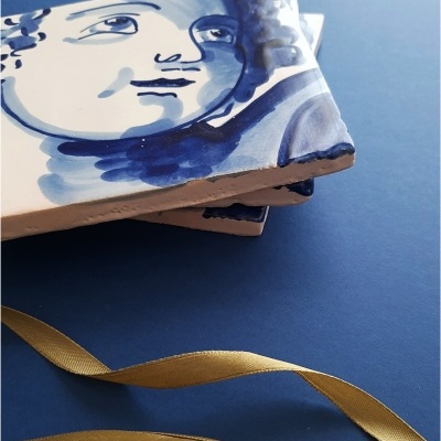 Azulejos de cerâmica com estampa azul e branca de rosto sobre superfície azul com fita dourada