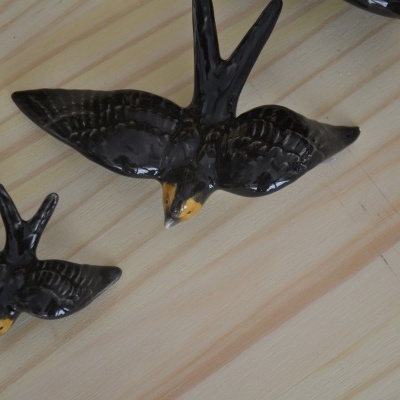 Pássaros de cerâmica preta e castanha sobre fundo de madeira clara