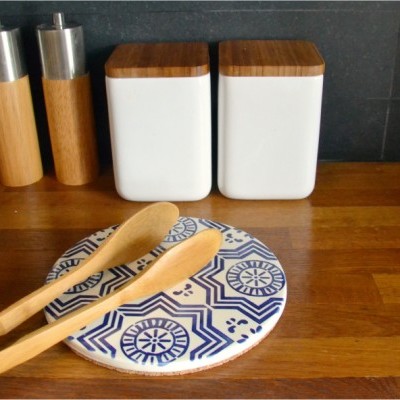 Utensílios de cozinha em bancada de madeira com recipientes brancos e tampas de madeira, moedores e espátulas sobre base decorada