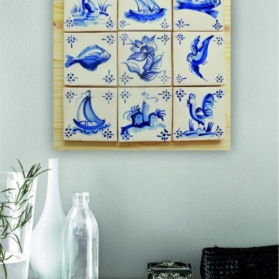 Painel de azulejos decorativos azuis e brancos com motivos variados pendurado na parede acima de mesa com decoração.