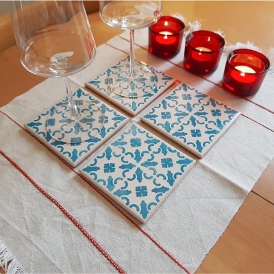 Azulejos azuis e brancos sobre tecido branco com copos de vidro e velas vermelhas acesas