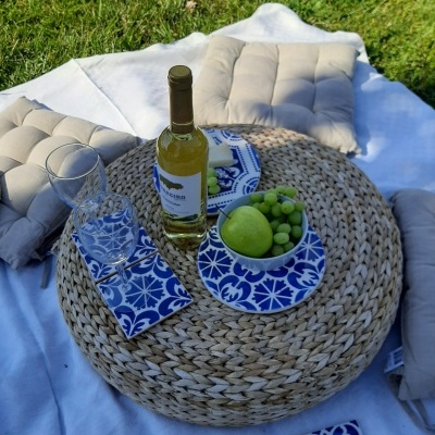 Mesa redonda de palha com garrafa de vinho e talheres em piquenique ao ar livre