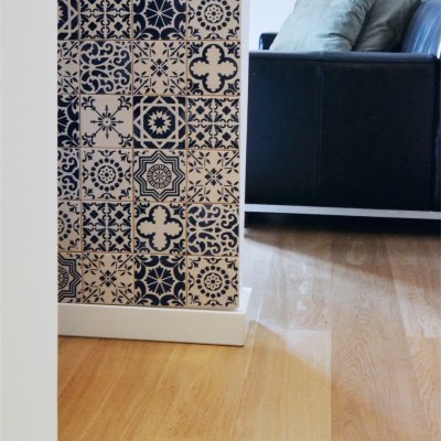 Parede com azulejos padrão geométrico azul e bege ao lado de sofá preto com almofadas cinzentas