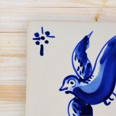 Azulejo branco com desenho azul de pássaro e padrão floral