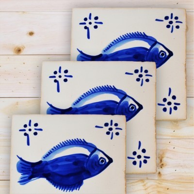 Três azulejos decorativos com peixes azuis em fundo branco