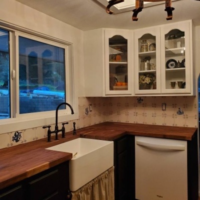 Rustic kitchen corner with white apron sink, wooden countertops, and black cabinets