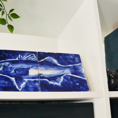 Prateleira branca com arte azul de peixe, plantas, livros e enfeites de gatos pretos