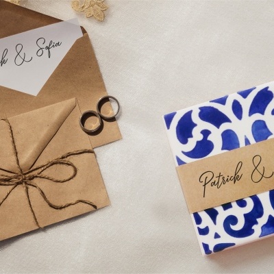 Convite de casamento com envelopes castanhos e cartão Patrick & Sofia ao lado de objeto embrulhado em papel azul e branco