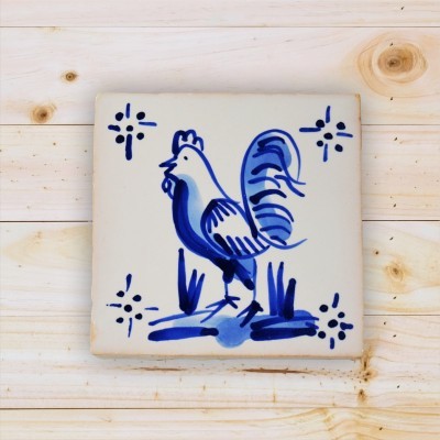 Azulejo cerâmico branco com desenho azul de galo sobre madeira clara