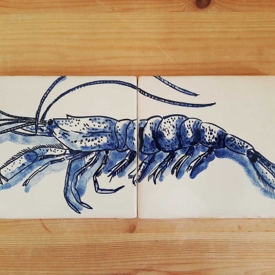 Dois azulejos brancos com desenho azul de crustáceo sobre madeira clara