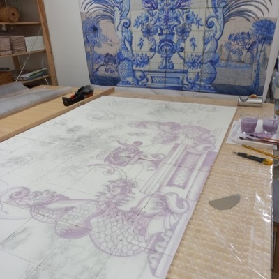 Painéis de azulejos azuis decorativos tradicionais e superfície de trabalho com desenhos em processo de pintura.