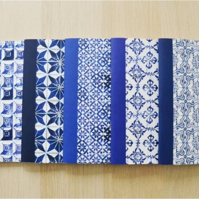 Seis cadernos azuis e brancos com padrões de azulejos sobre mesa de madeira.
