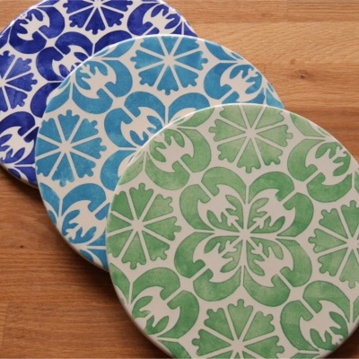 Três bases circulares com padrões florais em verde, azul claro e azul escuro sobre bancada de madeira