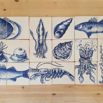 Azulejos brancos com desenhos azuis de animais marinhos e plantas sobre mesa de madeira