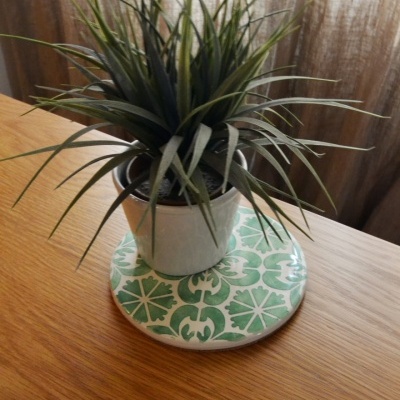 Vaso com planta artificial sobre suporte de cerâmica verde e branco em mesa de madeira
