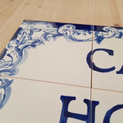 Azulejos de cerâmica branca pintados com azul e letras parciais sobre mesa de madeira