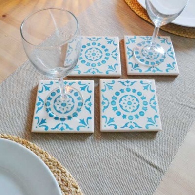 quatro bases de copo em cerâmica azuis e brancas numa mesa de madeira com copos e pratos