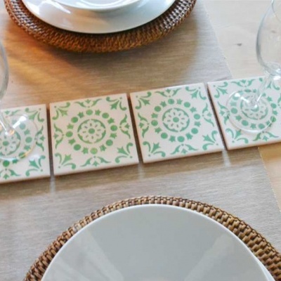 Quatro azulejos brancos com padrão verde, copos e pratos numa mesa