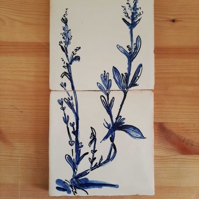 Dois azulejos brancos com pintura azul de planta sobre madeira clara