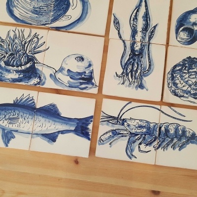 Azulejos brancos com desenhos azuis de animais marinhos e conchas sobre mesa de madeira.