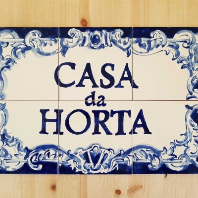Placa de azulejos com texto 'CASA da HORTA' em moldura azul sobre fundo de madeira