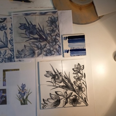Folhas com desenhos florais azuis e pretos sobre mesa branca com material de pintura