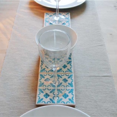 Mesa posta com pratos brancos, toalha bege e suportes de copo em azulejo azul e branco