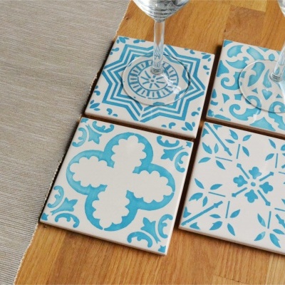 Quatro azulejos decorativos azuis e brancos sobre uma mesa de madeira com taças de vidro
