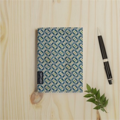 Caderno com capa azul e branca estampada em padrão geométrico sobre mesa de madeira com caneta e rama verde