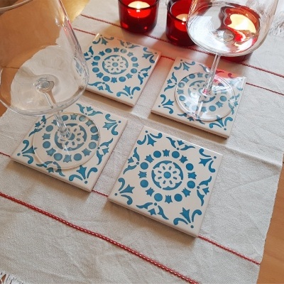 Conjunto de bases de copos em padrão azul e branco com duas taças de vinho e velas vermelhas numa mesa