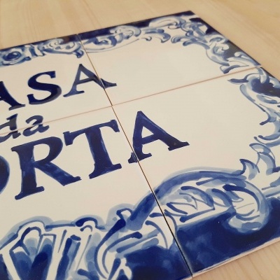 Placa decorativa de azulejos com texto 'CASA da PORTA' em azul sobre fundo branco com bordas azuis.