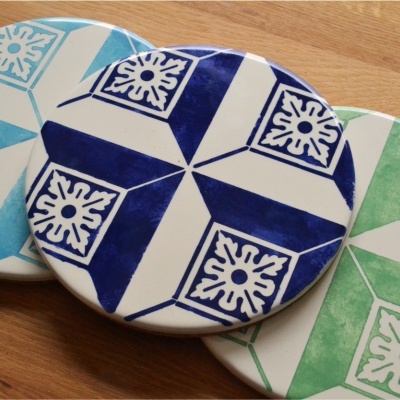 Bases para copos redondas com padrão geométrico em azul, verde e azul escuro sobre fundo de madeira