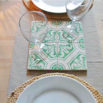 Mesa posta com pratos brancos, bases de palha, azulejos decorativos verdes e brancos e copos de vidro
