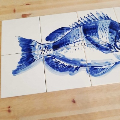 Seis azulejos brancos com desenho azul de peixe sobre madeira clara