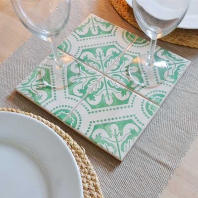 Azulejos quadrados decorativos verdes e brancos como suporte para copos numa mesa posta