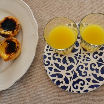 Dois copos de sumo de laranja num prato padrão azul e branco com croissant e pastéis de nata num pires branco