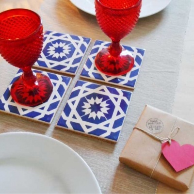 Azulejos azuis e brancos, copos vermelhos, prato branco e embalagem com etiqueta cor-de-rosa numa mesa de madeira