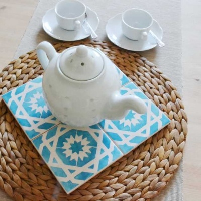 Conjunto de chá com bule branco em cerâmica e copos sobre base trançada e azulejo decorativo