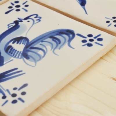 Azulejos decorativos azuis e brancos com desenho de galo e padrões florais sobre madeira clara