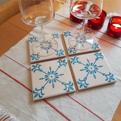 Bases de azulejo com padrão azul e taças de vidro sobre toalha com linhas vermelhas e velas acesas ao lado.