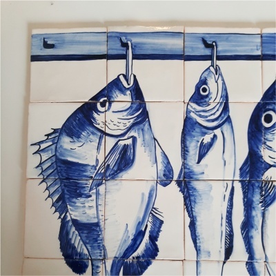 Azulejos azuis e brancos com desenho de peixes pendurados em ganchos.