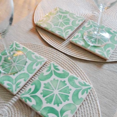 Bases quadradas de cerâmica verde e branca com copos de vidro sobre mesa de madeira