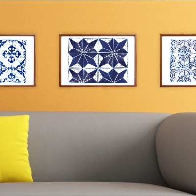 Três quadros com padrões azuis e brancos numa parede laranja acima de um sofá cinza com almofadas coloridas