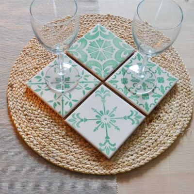 Azulejos de cerâmica com padrão verde e branco sobre descanso de palha com duas taças de vidro numa mesa de madeira