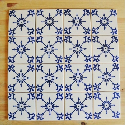Azulejos cerâmicos quadrados brancos com padrão azul em cruz dispostos sobre madeira clara
