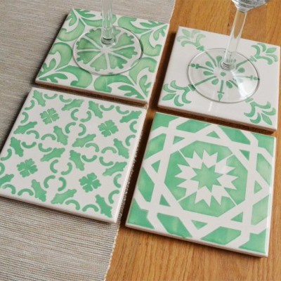 Azulejos quadrados verdes e brancos com padrões geométricos e florais sobre madeira clara